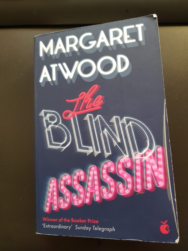 The Blind Assassin by Margaret Atwood is a magnificent and epic novel about a family in Canada in the first half of the last century. The story is excellently told by the oldest daughter Iris Chase. She is now in her eighties, disillusioned and somewhat cynical. She tells her story to her granddaughter Sabrina.
Iris grows up as one of two daughters of a wealthy factory owner who produces buttons. Iris’ granddad had established the factory back in the 1870s when buttons were in high demand. Iris has a sister Laura who is some years younger. The two sisters are despite that they are very different also very close as serious circumstances do that they only have each other to trust.